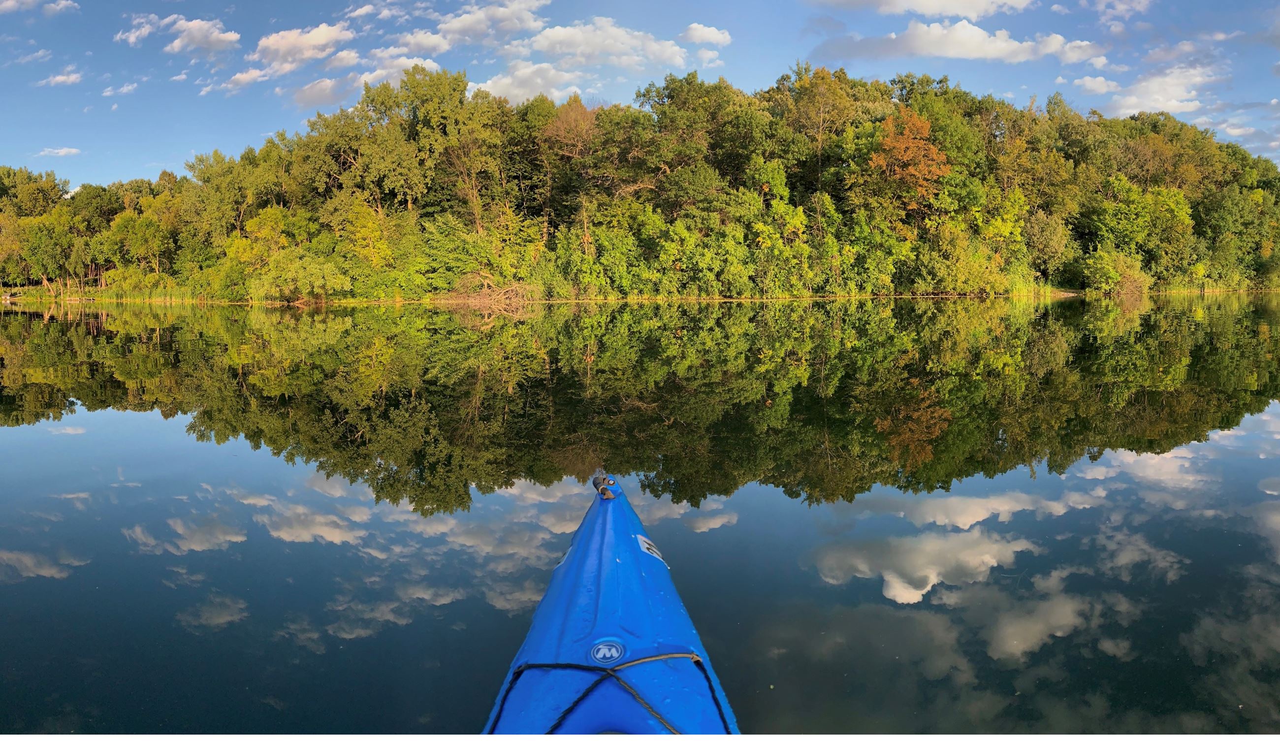 A blue kayak on a still lake, trees and sky reflected.