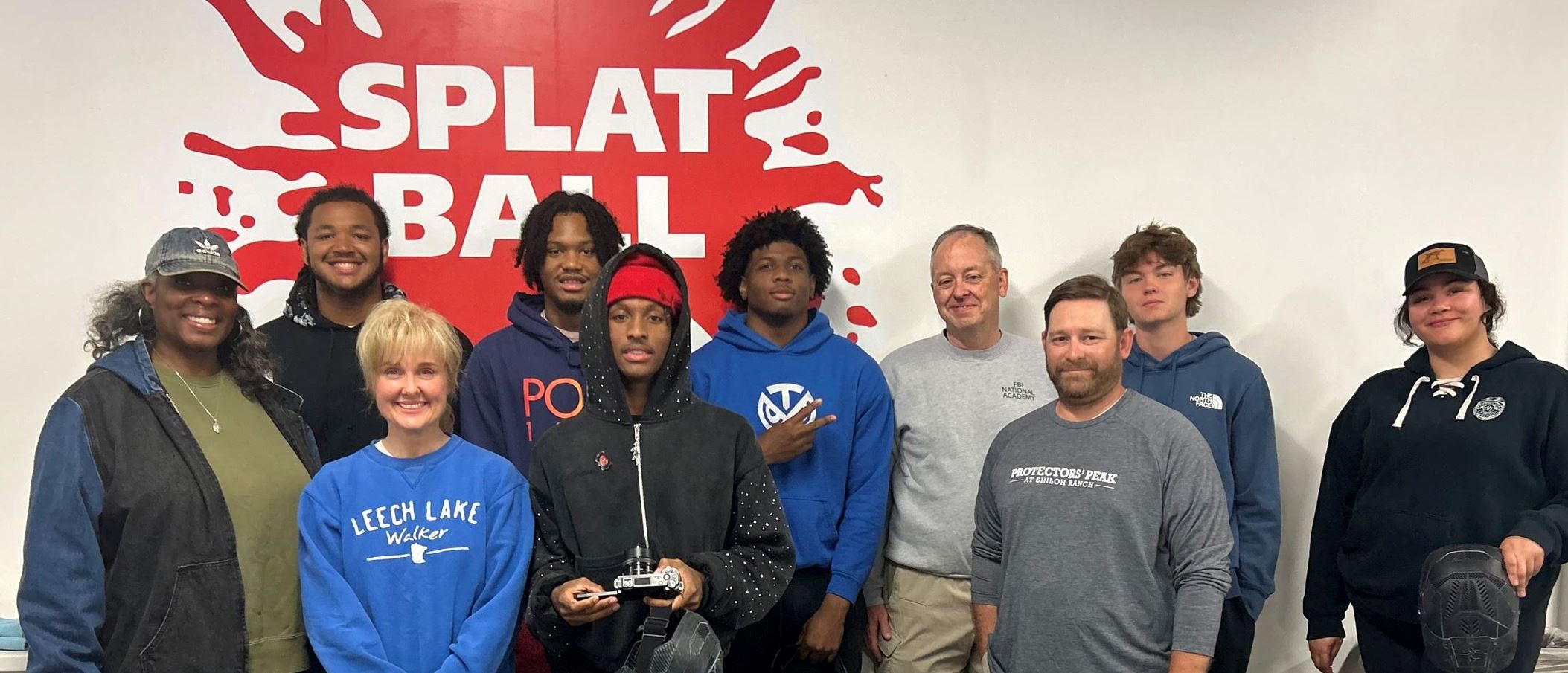 Officers with a group of teens posing in front of Splat Ball Sign