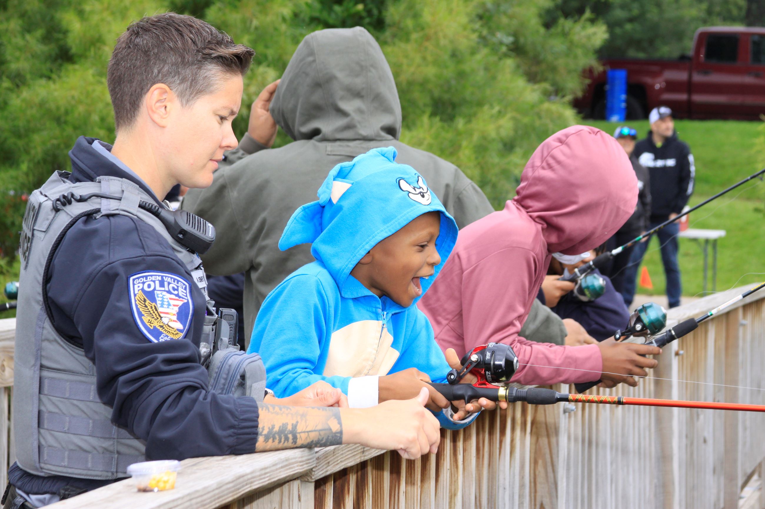 CSO Ashley Beimert stands next to a kid in a shark hoodie, and gives him pointers to help him fish